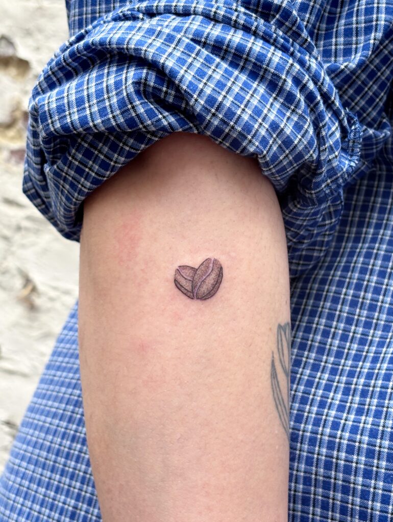 Image de portefolio, tatouage minimaliste de grains de café en fine line et ombrage sur l'avant-bras. 